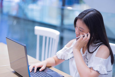 Girl talking on phone while using laptop on table