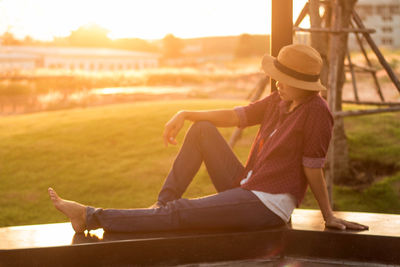 Side view of woman sitting on railing during sunset