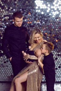 Woman in a gold dress sits with a newborn baby on a chair with her family