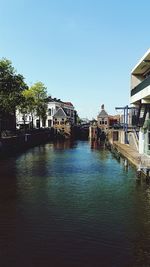 Canal amidst buildings against clear blue sky