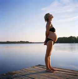 Pregnant woman standing on jetty at lake