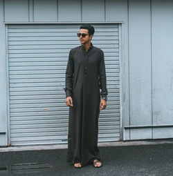 Man wearing sunglasses standing against closed shutter