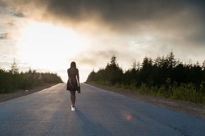 Rear view of woman waking on road against sky during sunset