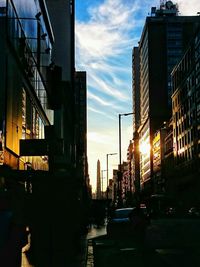 City street by buildings against sky during sunset