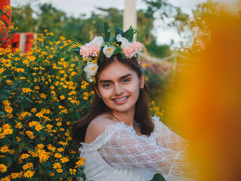 Portrait of smiling woman standing by yellow flowering plants