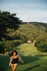 Smiling young woman running on field against sky