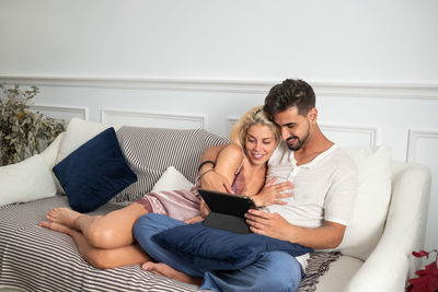Happy young couple cuddling and browsing tablet while sitting together on cozy sofa near table in the morning