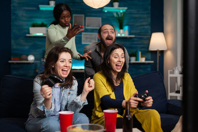 Portrait of smiling friends using mobile phone while sitting in cafe