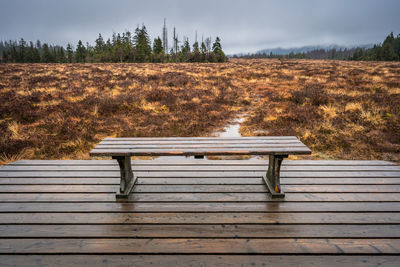 Empty bench on field against sky