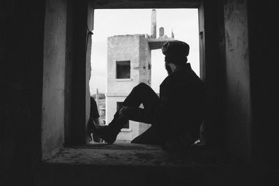 Side view of man sitting on window of abandoned building