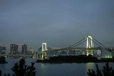 Rainbow bridge over bay of water in city against sky at dusk