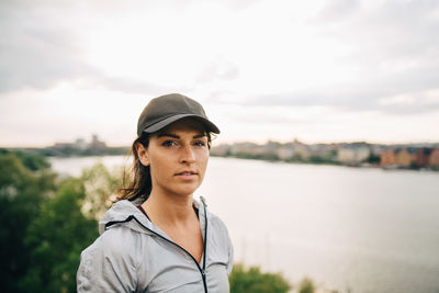 Portrait of confident female athlete standing on hill by sea against sky
