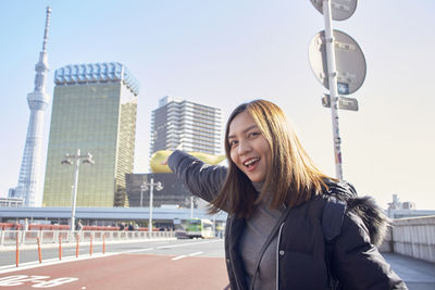 Portrait of smiling woman in city against sky