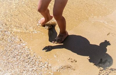 Low section of girl on shore at sandy beach during sunny day