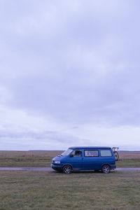 Car on road by field against sky