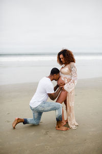 Mixed race couple on beach, kissing baby belly