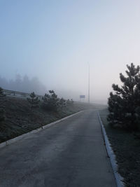 Empty road by trees against sky