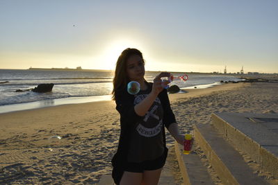Woman making bubbles at beach during sunset