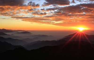 Scenic view of silhouette mountains against orange sky