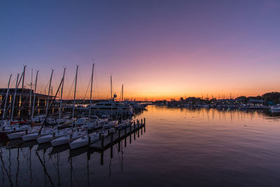 Sailboats moored in harbor at sunset