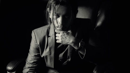 Portrait of young man sitting against black background