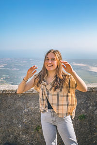 Portrait of young woman standing at beach against clear sky