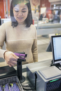 Smiling young woman paying through smart phone at checkout counter in supermarket
