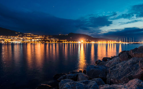 Illuminated city by sea against sky at night