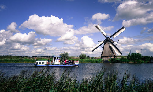 Traditional windmill by lake against sky