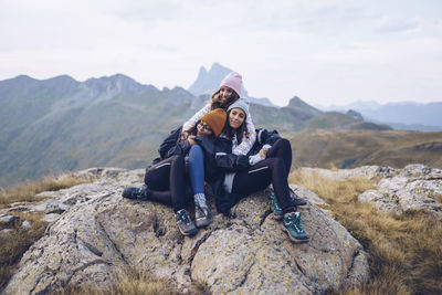 Friends embracing while sitting on rock around ibones of anayet