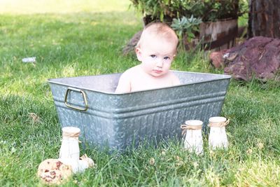 A small boy looking at the camera while relaxing in a tin tub in the yard.