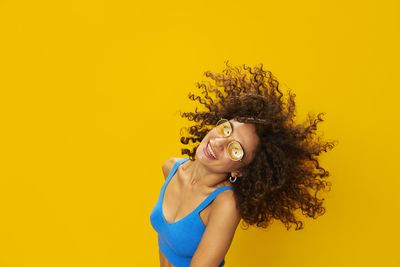 Portrait of smiling young woman standing against yellow background