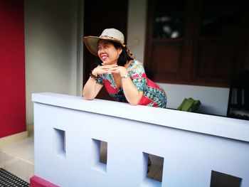 Smiling mature woman wearing hat while leaning on railing