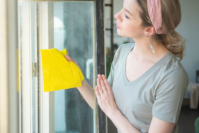 Beautiful woman wiping window at home