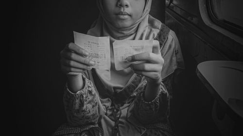 Midsection of woman holding paper while sitting in bus