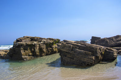 Rock formations by sea against clear blue sky