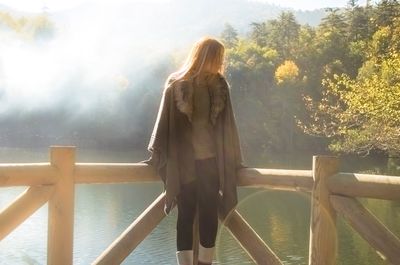 Rear view of woman standing by railing against sea