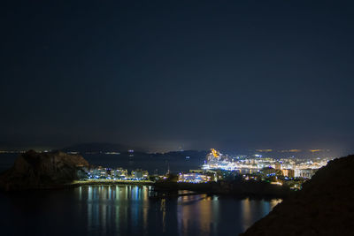 Illuminated buildings by sea against sky at night