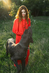 Portrait of young woman with dog on grassy field