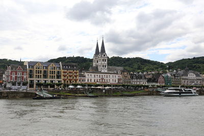 Buildings at waterfront against cloudy sky