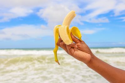 Cropped image of hand holding banana against sea