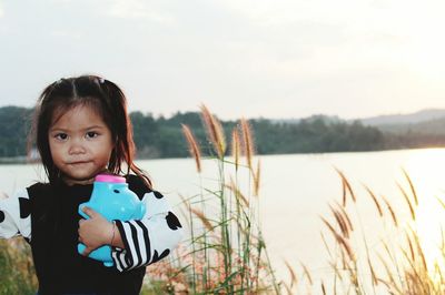 Portrait of girl standing with piggy bank against clear sky