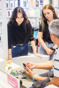 Young female trainees looking at mobile phone while listening to male owner sitting at desk in repair shop