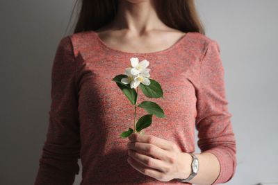 Midsection of woman holding red while standing against wall