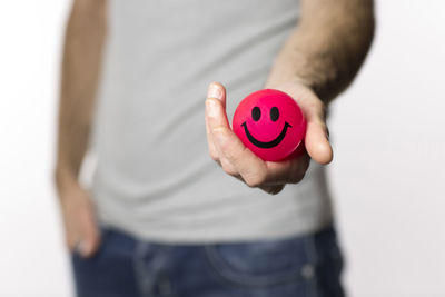 Midsection of man holding red ball with smiley face against white background