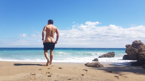 Rear view of shirtless man standing on beach