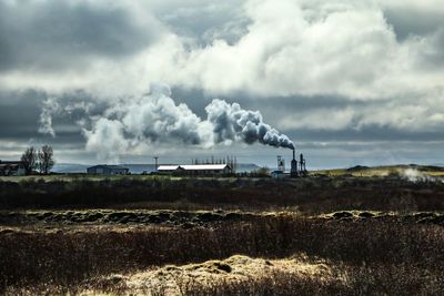 Smoke emitting from factory against cloudy sky