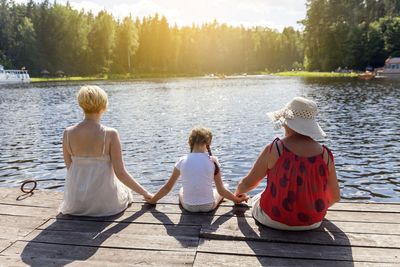 Rear view of girl sitting with mother and grandmother on pier over lake