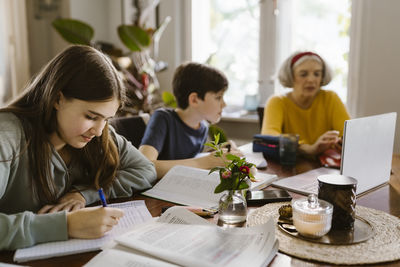 Girl doing homework while sitting with brother and grandmother at home