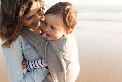 Smiling mother carrying son while standing at beach